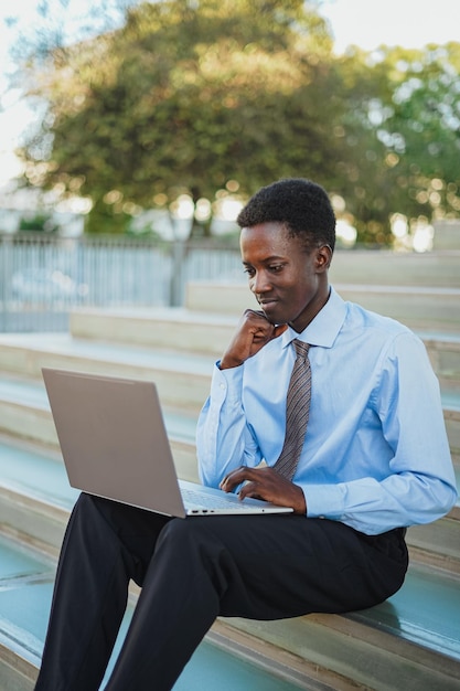 Hombre de negocios africano sonriente trabajando con su computadora portátil Está sentado en las escaleras