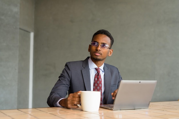 Hombre de negocios africano con traje y corbata en una cafetería mientras usa una computadora portátil