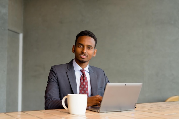 Hombre de negocios africano con traje y corbata en una cafetería mientras usa una computadora portátil