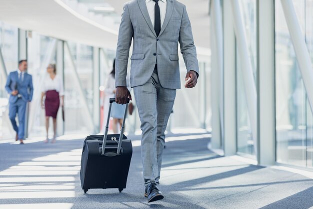 Un hombre de negocios afroamericano caminando por el pasillo con una maleta en una oficina moderna.