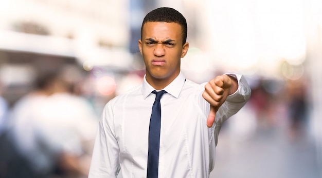 El hombre de negocios afroamericano joven que muestra el pulgar abajo firma con la expresión negativa en la ciudad