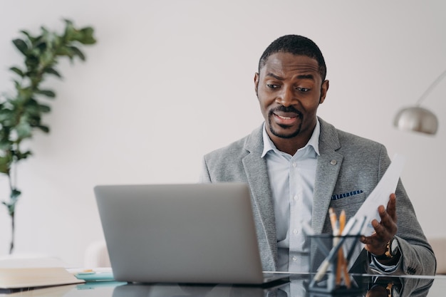 Hombre de negocios afroamericano perplejo mirando la pantalla del portátil leyendo malas noticias en el correo electrónico en el escritorio