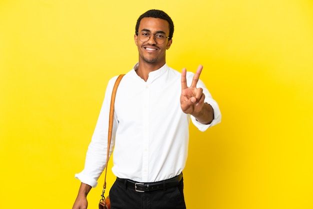 Hombre de negocios afroamericano sobre fondo amarillo aislado sonriendo y mostrando el signo de la victoria