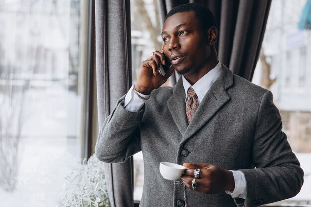El hombre de negocios afroamericano tiene una conversación en un teléfono inteligente y una taza de café