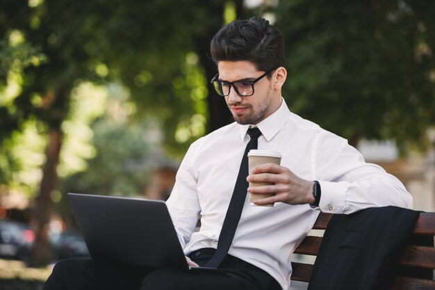 Hombre de negocios al aire libre en el parque con ordenador portátil tomando café.