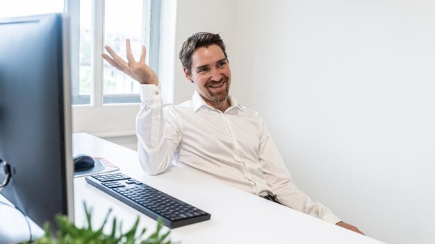 Un hombre de negocios alegre sentado en su escritorio con una computadora explicando algo