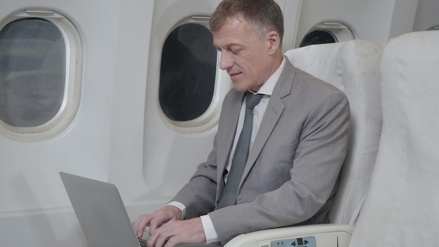 Hombre de negocios de alto nivel en una aerolínea de primera clase trabajando en su computadora portátil