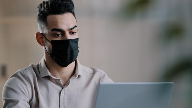 Hombre de negocios árabe enfermo en programador diseñador de máscaras médicas escribiendo en información de búsqueda de portátiles