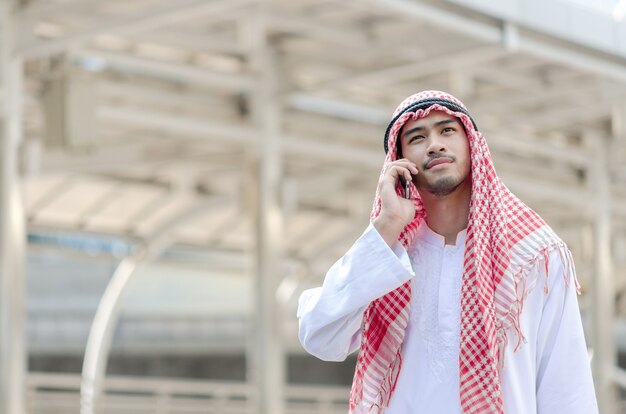 Hombre de negocios árabe joven que usa el teléfono móvil mientras que camina en la ciudad.