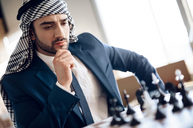 Hombre de negocios árabe que juega a ajedrez en la tabla en la habitación.