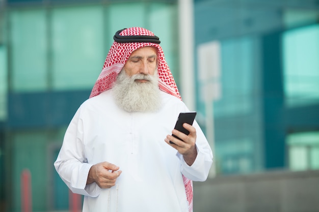 Hombre de negocios árabe trabajando con su teléfono en una calle en el fondo