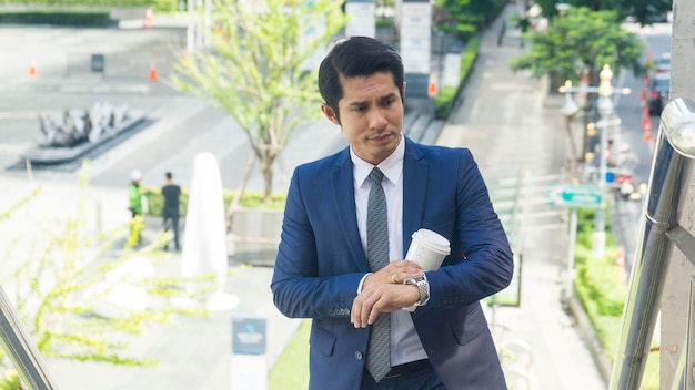 Hombre de negocios de asia de pie con vaso de papel de bebida en la pasarela de la escalera peatonal al aire libre