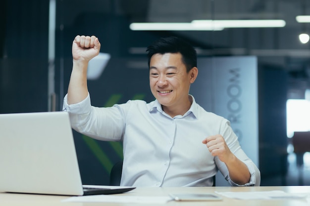 Hombre de negocios asiático alegre y exitoso bailando en la oficina celebrando el triunfo