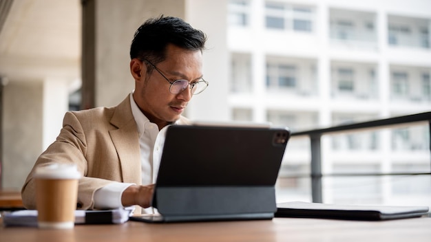 Un hombre de negocios asiático concentrado está trabajando en su tableta digital y revisando un documento de negocios