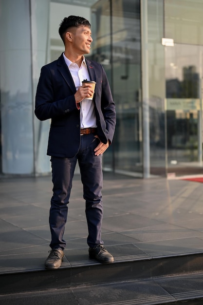 Hombre de negocios asiático confiado en un traje de negocios formal de pie frente al edificio de la empresa