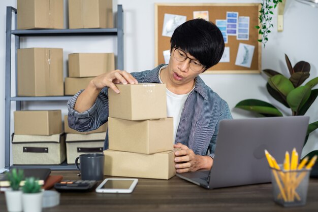 Hombre de negocios asiático emprendedor PYME o autónomo que trabaja en una caja de cartón prepara la caja de entrega para el cliente