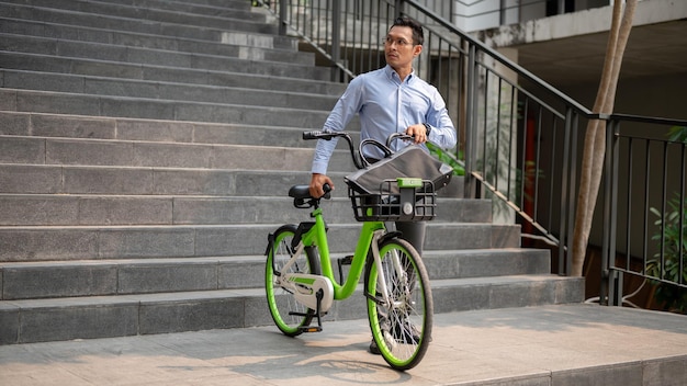 Foto un hombre de negocios asiático enfocado empujando una bicicleta verde en la ciudad yendo a trabajar con su bicicleta