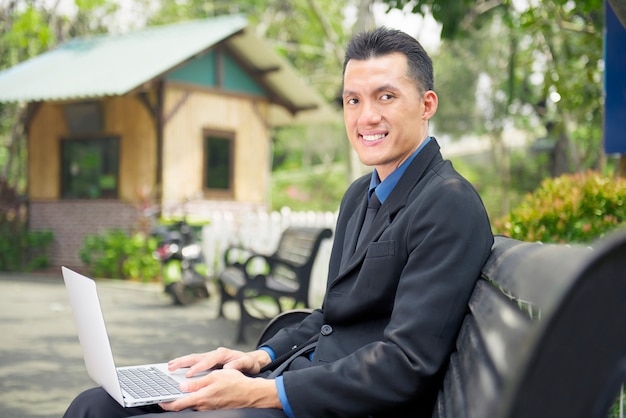 Hombre de negocios asiático feliz que se sienta y que usa el ordenador portátil