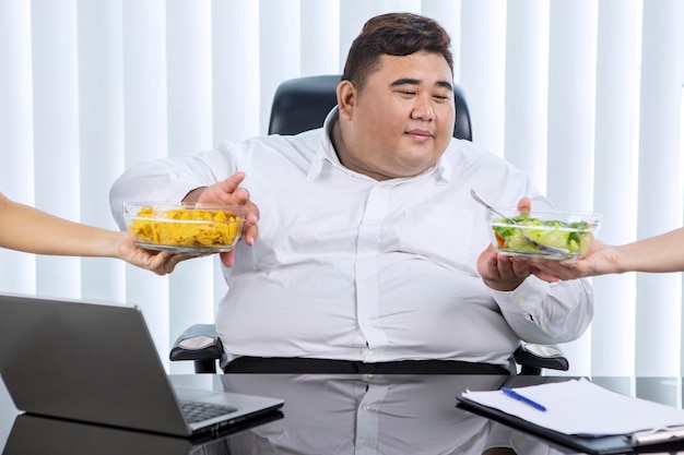 Hombre de negocios asiático gordo que prefiere la ensalada sobre las patatas fritas