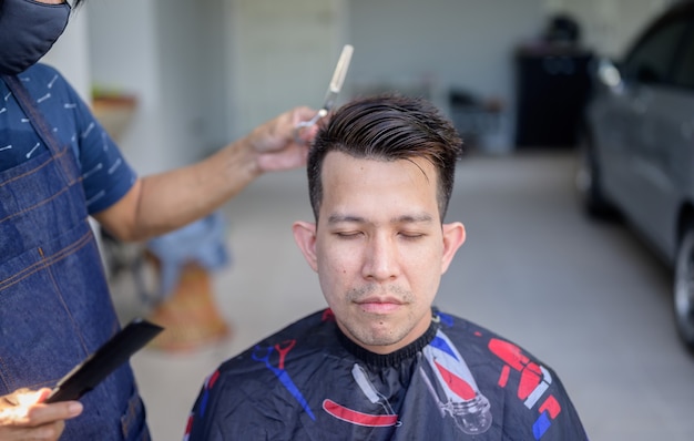 Hombre de negocios asiático haciendo corte de pelo y salón en casa. Peluquería al aire libre en el jardín. Distanciamiento social y nuevo estilo de vida normal.