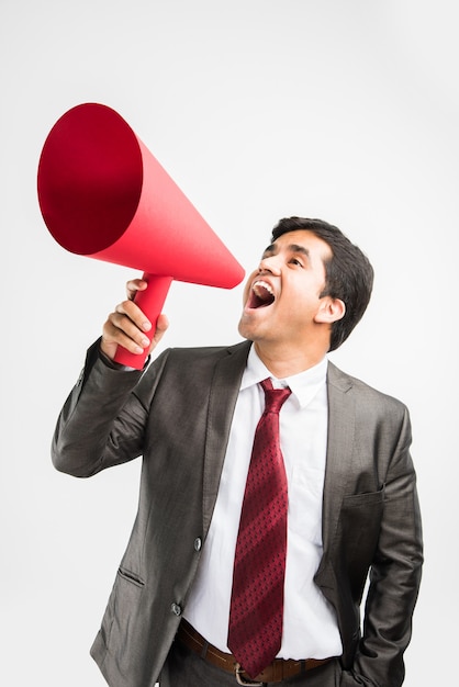 Hombre de negocios asiático indio que anuncia o difunde noticias utilizando un altavoz rojo o un mega micrófono hecho de papel, aislado sobre fondo blanco.