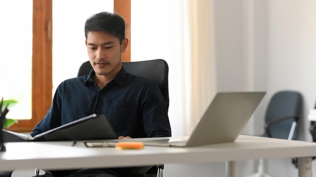 Un hombre de negocios asiático inteligente y profesional lee y examina un informe de negocios en su escritorio de oficina