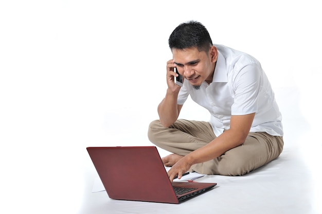 El hombre de negocios asiático joven o el empresario asiático joven se sienta en el piso blanco que sostiene la computadora portátil. Emocionado por el joven autónomo asiático. Concepto emocionado.