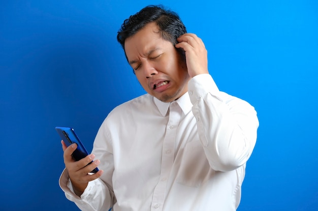 Hombre de negocios asiático leyendo mensajes de texto charlando en su teléfono, malas noticias, expresión de llanto triste. fondo azul