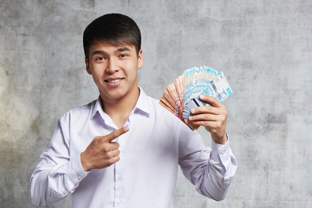 Hombre de negocios asiático con montón de tenge kazajo en mano. El empresario exitoso ha ganado mucho dinero en transacciones y venta de acciones.