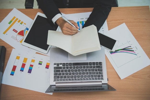 Hombre de negocios asiático que trabaja en el escritorio con una computadora portátil, una tableta y un teléfono inteligente desde la vista superior