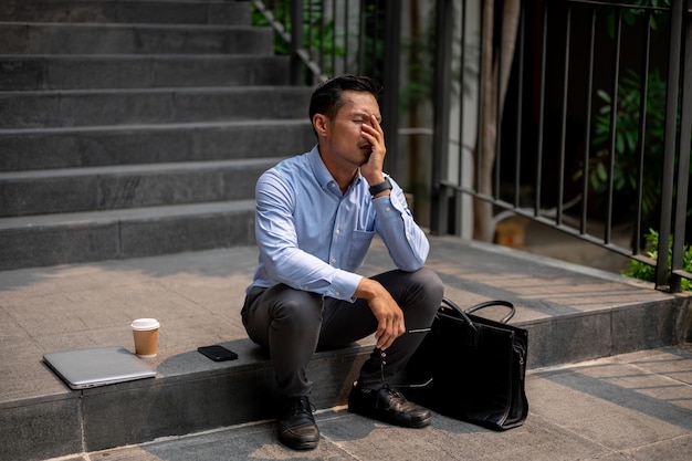 Foto un hombre de negocios asiático se sienta en las escaleras al aire libre experimentando frustración y el miedo de ser despedido