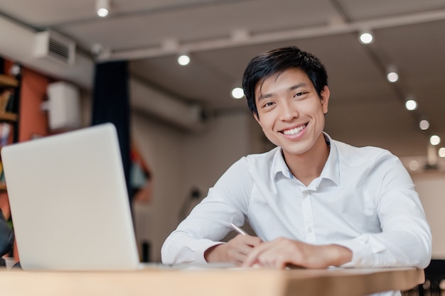 Hombre de negocios asiático sonriente en la oficina de la compañía con la computadora portátil