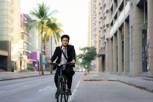 Hombre de negocios asiático en traje está montando una bicicleta en las calles de la ciudad para su viaje diario al trabajo