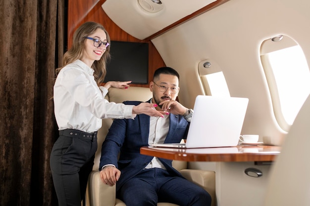 Un hombre de negocios asiático con traje y gafas vuela en un avión privado de lujo con una colega