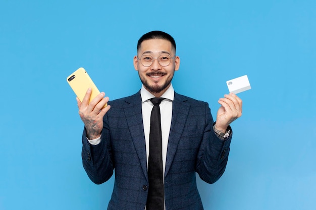 hombre de negocios asiático en traje tiene teléfono inteligente y tarjeta de crédito con fondo azul empresario coreano