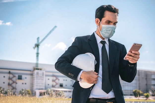 Hombre de negocios asiático usar mascarilla llamar teléfono al aire libre en la construcción del sitio