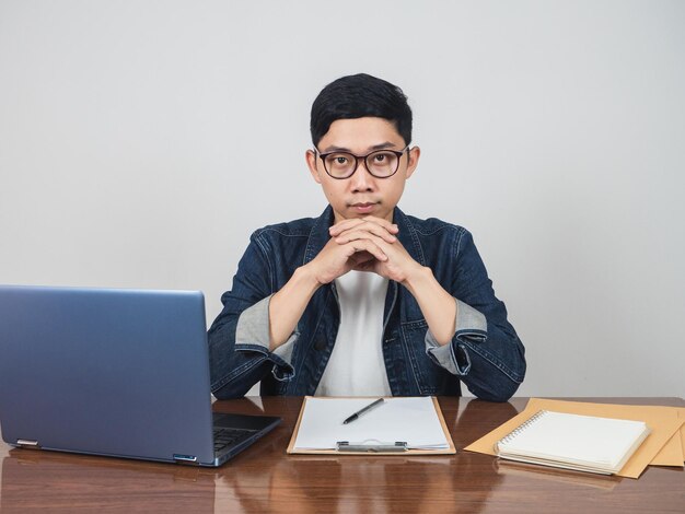 El hombre de negocios asiático se ve confiado sentado en la mesa del lugar de trabajo mirándote