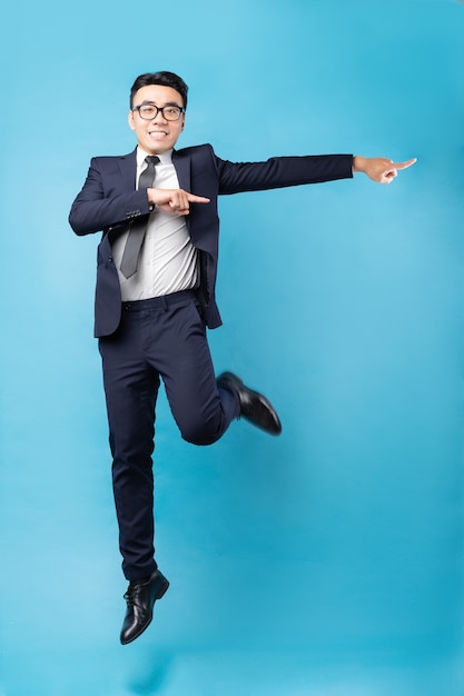 Hombre de negocios asiático vistiendo traje y saltar sobre la pared azul