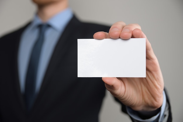 Hombre de negocios, asimiento de la mano del hombre de negocios que muestra la tarjeta de visita - primer plano sobre fondo gris. Muestre una hoja de papel en blanco. Tarjeta de visita en papel.