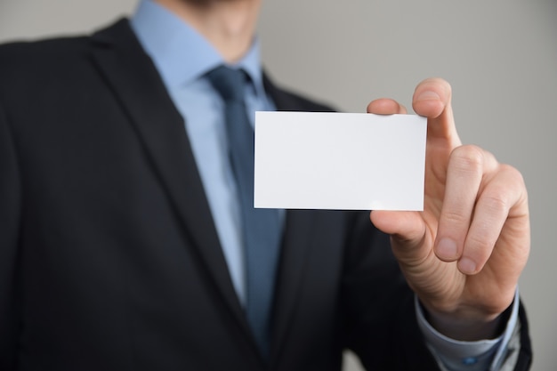 Hombre de negocios, asimiento de la mano del hombre de negocios que muestra la tarjeta de visita - primer plano sobre fondo gris. Muestre una hoja de papel en blanco. Tarjeta de visita en papel.