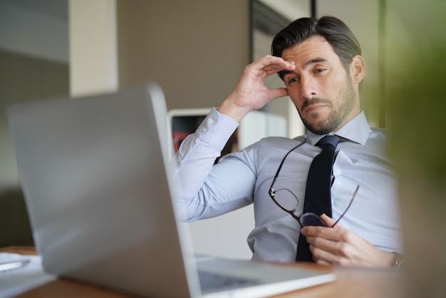 Hombre de negocios atractivo que parece preocupado y cansado delante del ordenador portátil