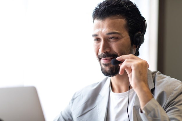 Hombre de negocios atractivo en trajes y auriculares sonriendo mientras trabaja en el escritorio