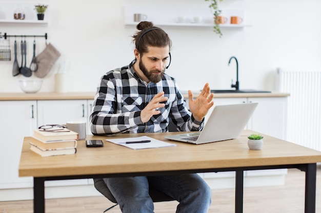 Hombre de negocios con auriculares gestando frente a la computadora mientras hace trabajo en casa