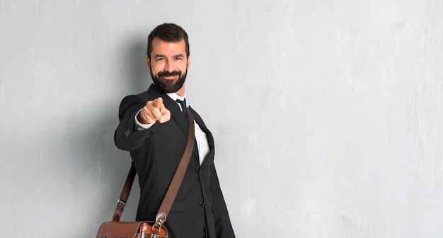 Hombre de negocios con barba apunta el dedo hacia ti con una expresión de confianza