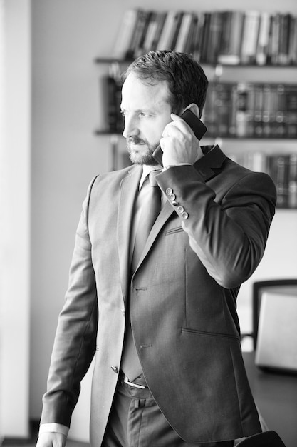 Hombre de negocios con barba en traje formal azul hablar por teléfono móvil en el escritorio del lugar de trabajo en la oficina Concepto de comunicación empresarial