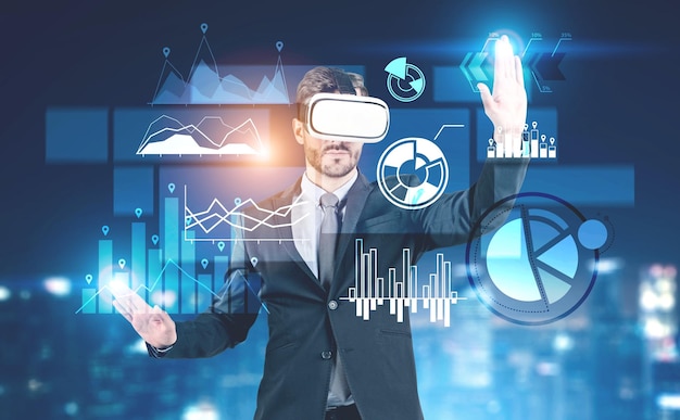 Hombre de negocios con barba con traje oscuro y gafas VR interactuando con la interfaz de infografías de negocios sobre un fondo borroso.