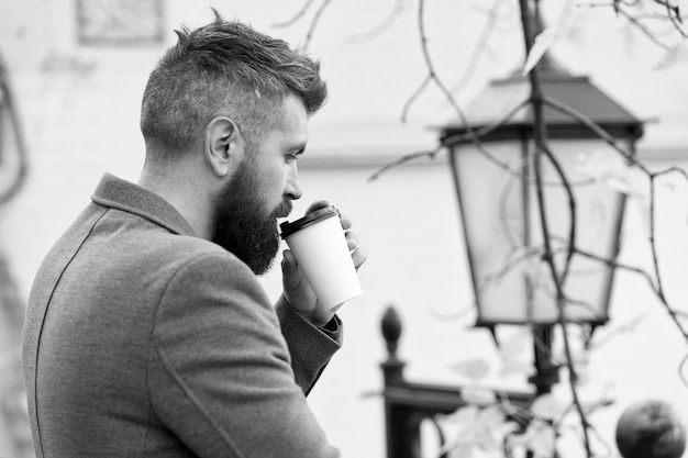Hombre de negocios barbudo bebe café al aire libre Hipster sostiene una taza de café de papel y disfruta del entorno del parque Relajante descanso para tomar café Bébelo mientras viajas Hombre barbudo hipster prefiere café para llevar