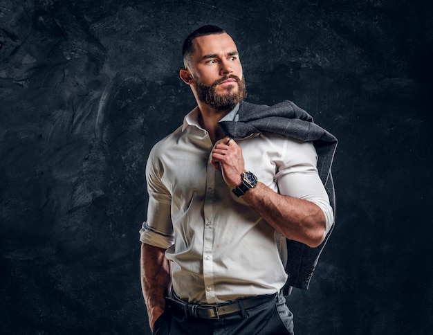 Foto un hombre de negocios barbudo y pensativo con camisa blanca posa para el fotógrafo sobre un fondo oscuro.