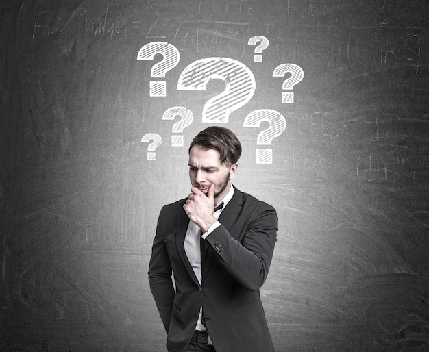 Un hombre de negocios barbudo con traje está parado cerca de una pizarra con múltiples bocetos de signos de interrogación. Bosquejo