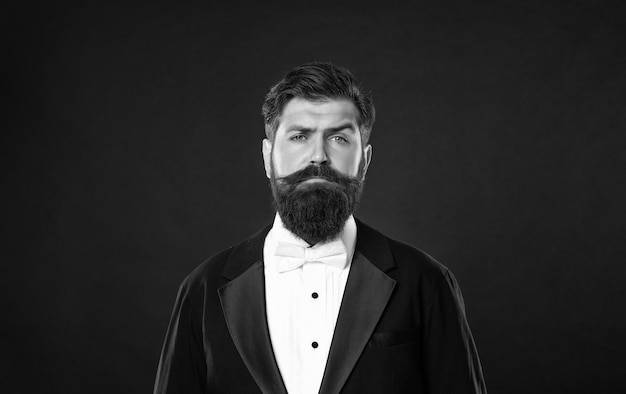 Un hombre de negocios barbudo en tuxedo con ropa masculina de fondo negro.